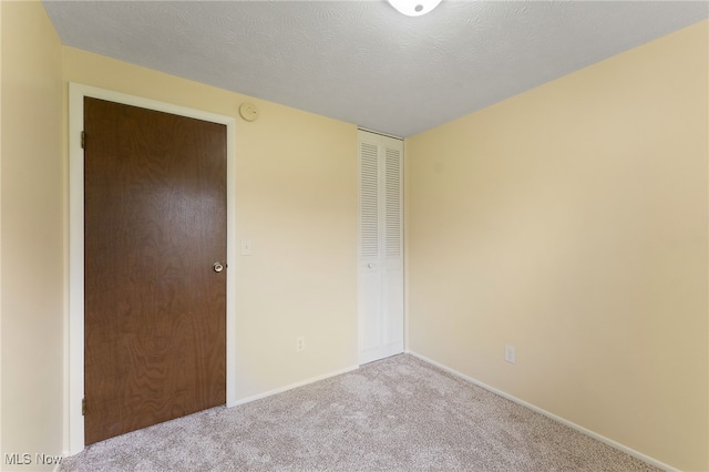 unfurnished bedroom featuring light carpet, a textured ceiling, and a closet