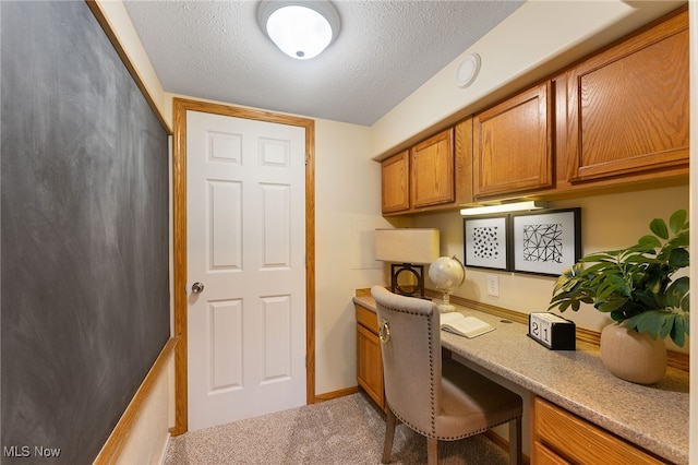 carpeted home office featuring built in desk and a textured ceiling