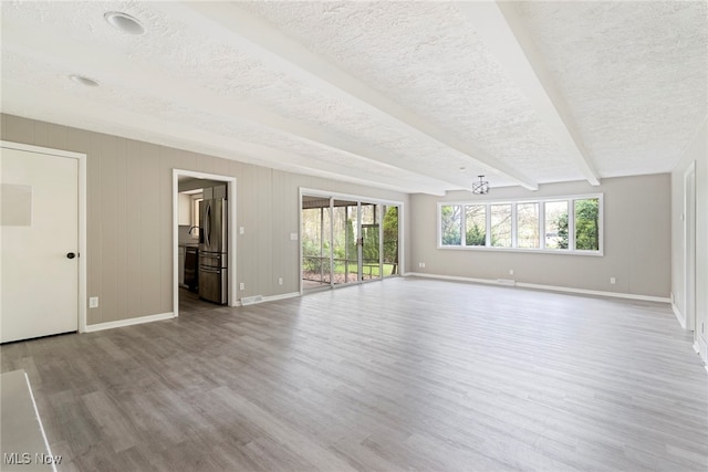 interior space with light wood-type flooring, beam ceiling, and a textured ceiling