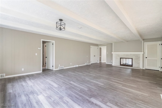 unfurnished living room featuring a textured ceiling, beam ceiling, and hardwood / wood-style floors