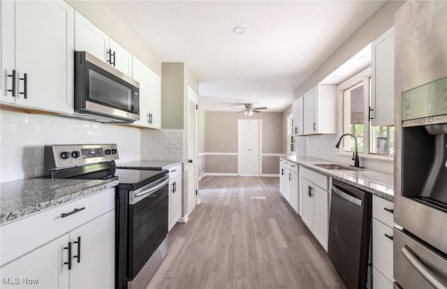 kitchen with light stone counters, white cabinets, sink, appliances with stainless steel finishes, and light wood-type flooring