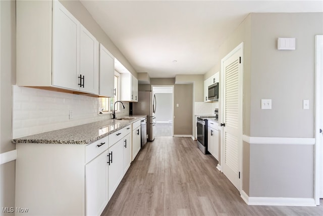 kitchen with white cabinetry, stone countertops, stainless steel appliances, light hardwood / wood-style flooring, and sink