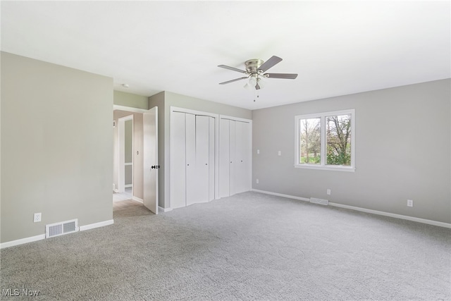 unfurnished bedroom with ceiling fan, light colored carpet, and two closets