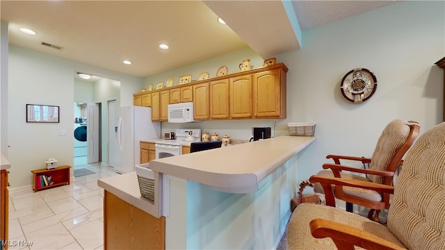 kitchen with white appliances, kitchen peninsula, and washer / dryer