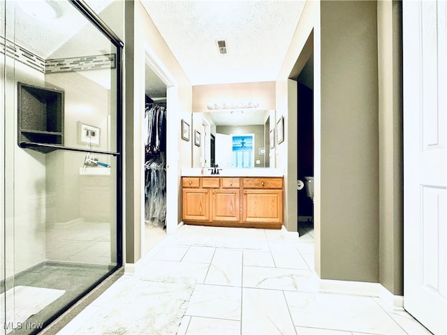 bathroom with a shower with door, vanity, and a textured ceiling