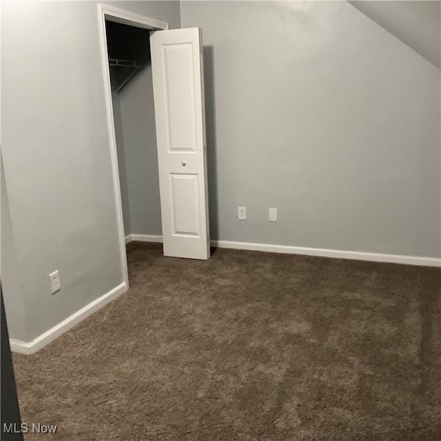 unfurnished bedroom with dark carpet, a closet, and vaulted ceiling