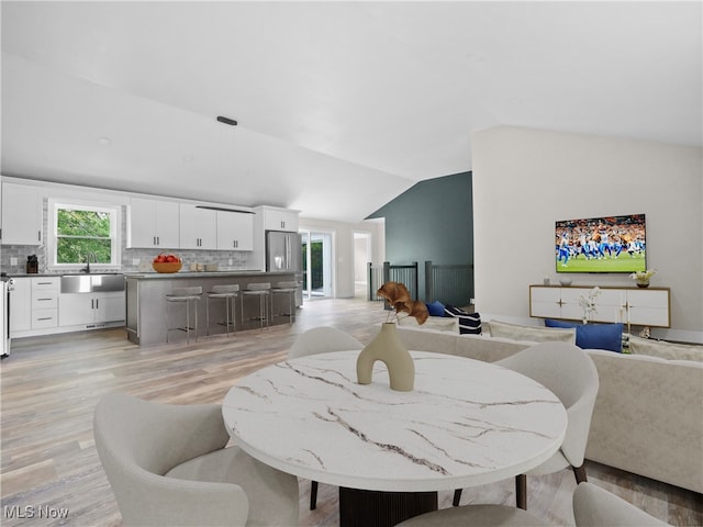 dining room featuring sink, light hardwood / wood-style floors, and vaulted ceiling