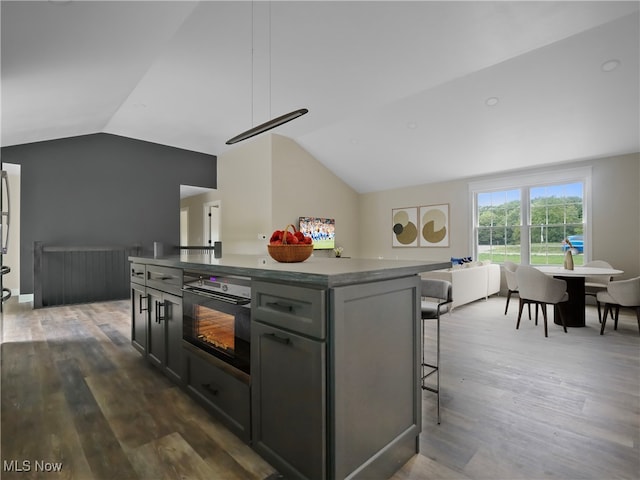 kitchen with a breakfast bar, vaulted ceiling, a kitchen island, dark hardwood / wood-style floors, and black oven