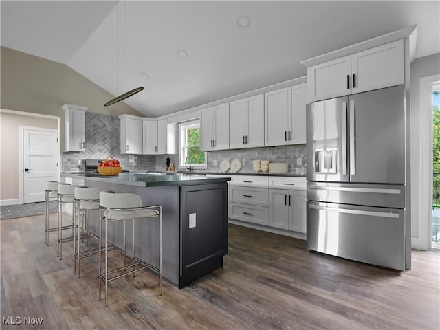 kitchen featuring a kitchen bar, stainless steel refrigerator with ice dispenser, white cabinets, dark hardwood / wood-style floors, and lofted ceiling