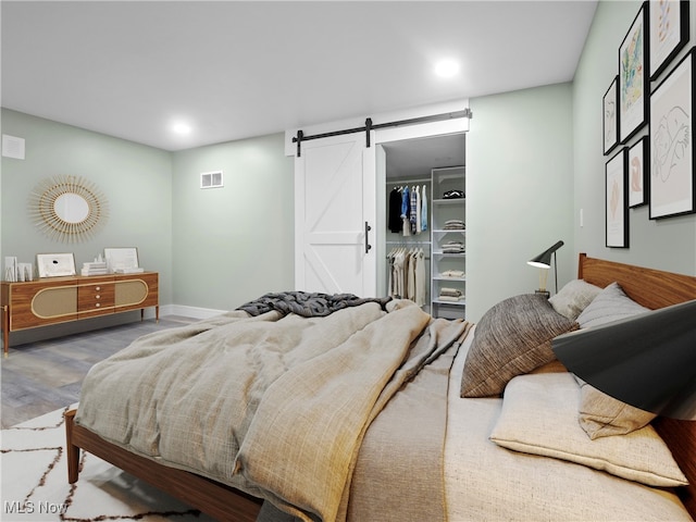 bedroom featuring a walk in closet, wood-type flooring, a barn door, and a closet