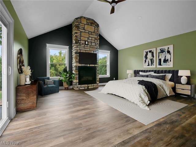 bedroom featuring lofted ceiling, access to outside, a stone fireplace, hardwood / wood-style flooring, and ceiling fan