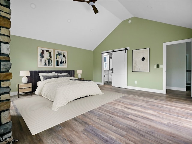 bedroom featuring high vaulted ceiling, ensuite bath, hardwood / wood-style flooring, ceiling fan, and a barn door