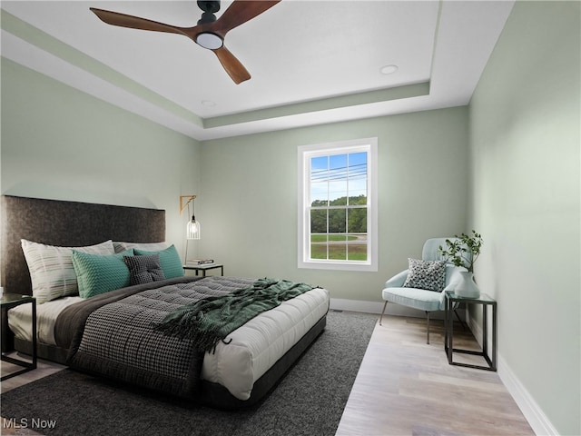 bedroom with a tray ceiling, ceiling fan, and light wood-type flooring