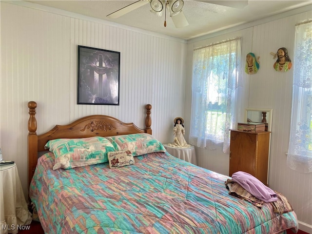 bedroom with a textured ceiling, ceiling fan, and wooden walls