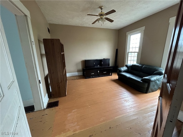 living room featuring light wood-type flooring, a textured ceiling, and ceiling fan