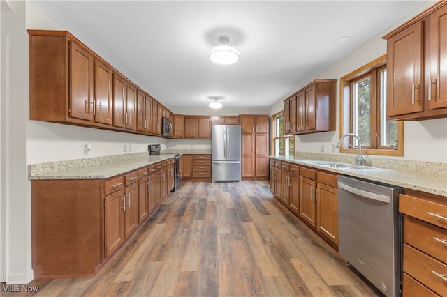 kitchen with wood-type flooring, sink, stainless steel appliances, and light stone countertops