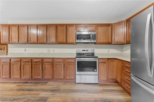 kitchen with light stone counters, appliances with stainless steel finishes, and light hardwood / wood-style floors