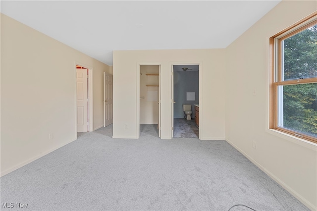 unfurnished bedroom featuring light carpet, multiple windows, a spacious closet, and ensuite bathroom