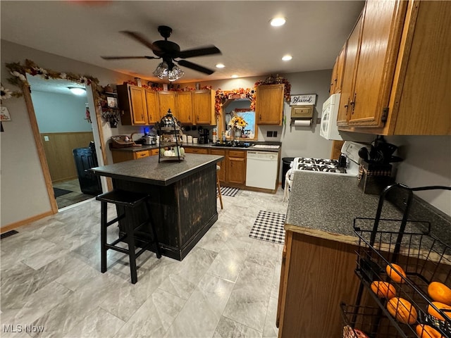 kitchen featuring white appliances, a kitchen island, a breakfast bar area, ceiling fan, and sink