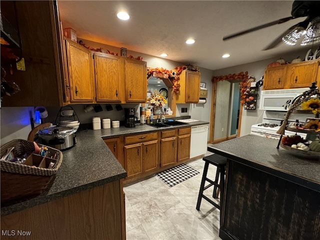 kitchen featuring ceiling fan, a kitchen bar, sink, and white appliances