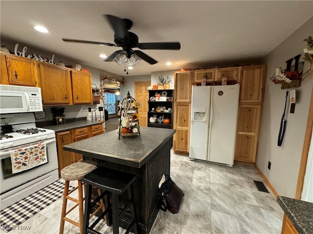 kitchen featuring white appliances, a kitchen island, ceiling fan, and a breakfast bar