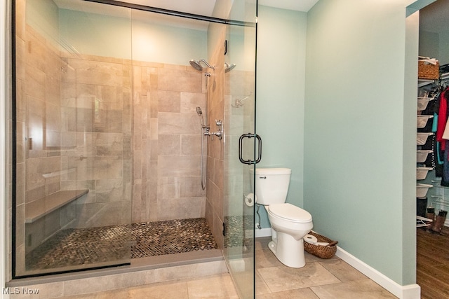 bathroom featuring a shower with door, toilet, and tile patterned flooring