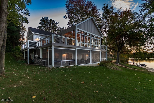 back house at dusk featuring a lawn and a sunroom