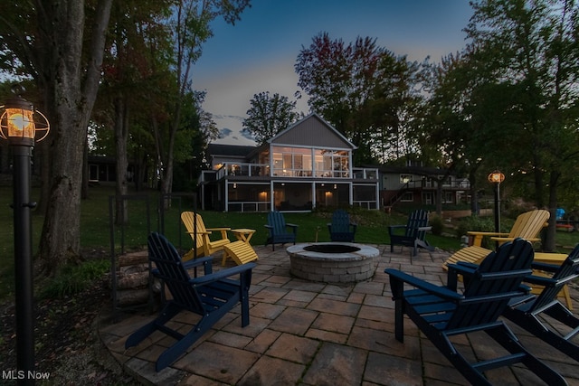 patio terrace at dusk with a yard, a fire pit, and a sunroom