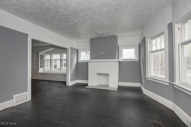 unfurnished living room with a brick fireplace, a textured ceiling, and dark hardwood / wood-style flooring