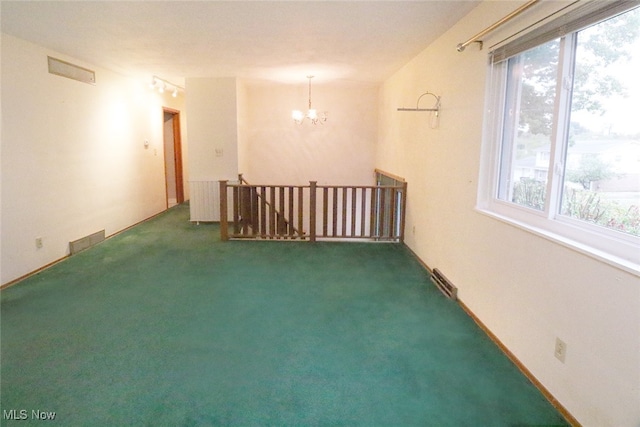 carpeted empty room with plenty of natural light and a chandelier