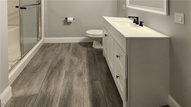 bathroom featuring vanity, hardwood / wood-style floors, a shower with shower door, and toilet