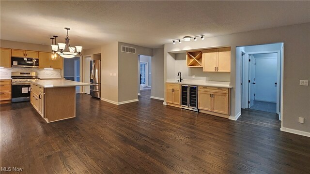 kitchen with appliances with stainless steel finishes, dark hardwood / wood-style flooring, light brown cabinetry, beverage cooler, and decorative light fixtures