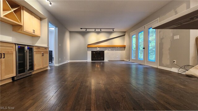 unfurnished living room with beverage cooler, track lighting, indoor bar, and dark hardwood / wood-style flooring