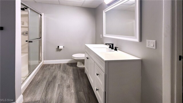 bathroom featuring a paneled ceiling, walk in shower, hardwood / wood-style floors, vanity, and toilet