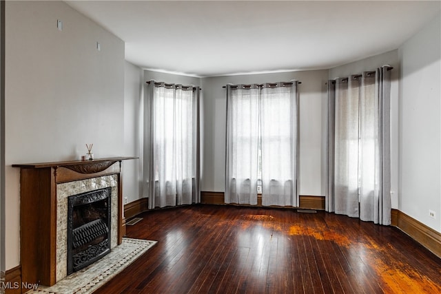 unfurnished living room with dark wood-type flooring, a high end fireplace, and a wealth of natural light