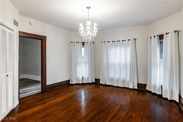 empty room with a notable chandelier and dark hardwood / wood-style flooring