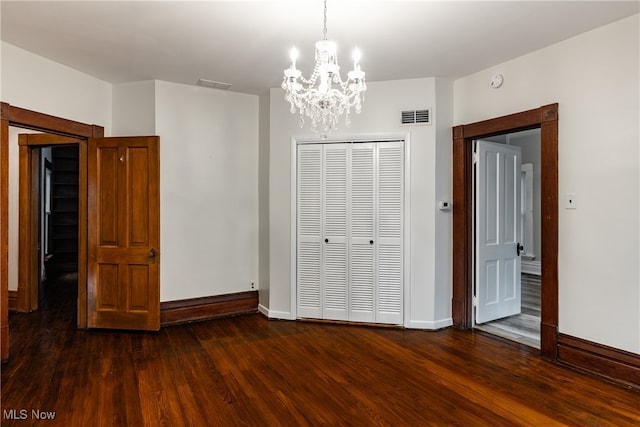 unfurnished bedroom featuring an inviting chandelier, dark wood-type flooring, and a closet