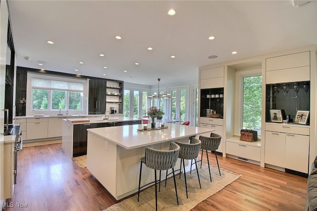 kitchen featuring white cabinets, light hardwood / wood-style floors, hanging light fixtures, a kitchen island, and a breakfast bar