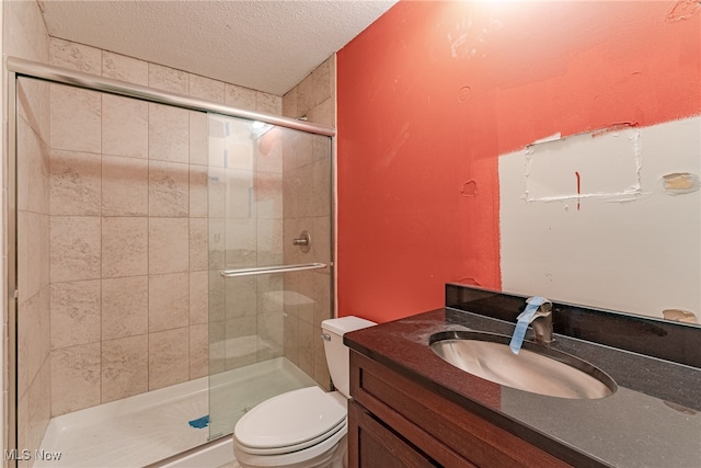 bathroom with a textured ceiling, an enclosed shower, vanity, and toilet