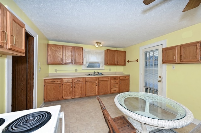 kitchen with a textured ceiling, white stove, ceiling fan, and sink