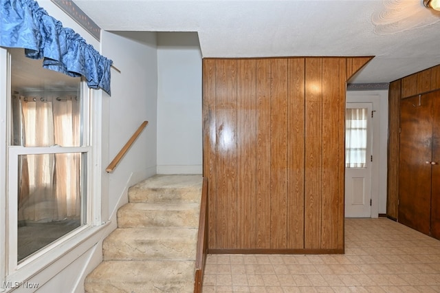 staircase featuring a textured ceiling and wooden walls