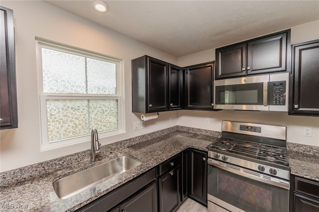 kitchen featuring a textured ceiling, appliances with stainless steel finishes, sink, and dark stone counters