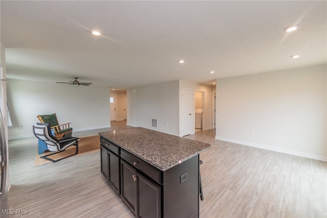 kitchen featuring ceiling fan, light hardwood / wood-style flooring, stone counters, and a kitchen island