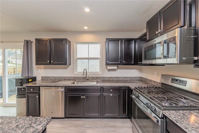 kitchen with dark stone counters, stainless steel appliances, light wood-type flooring, and sink