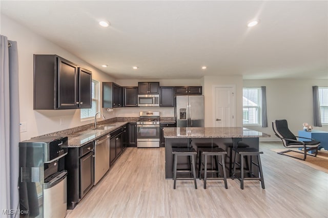 kitchen with light wood-type flooring, a kitchen island, appliances with stainless steel finishes, a kitchen breakfast bar, and light stone countertops