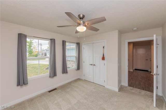 unfurnished bedroom with light carpet, a closet, ceiling fan, and a textured ceiling