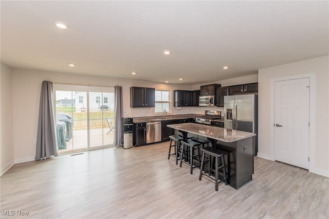 kitchen featuring light stone counters, a kitchen island, light hardwood / wood-style flooring, stainless steel appliances, and a kitchen breakfast bar