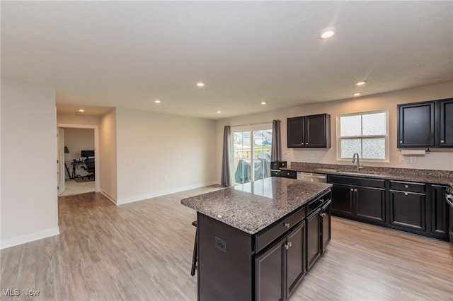 kitchen with dark stone countertops, light wood-type flooring, a kitchen bar, a center island, and stainless steel dishwasher