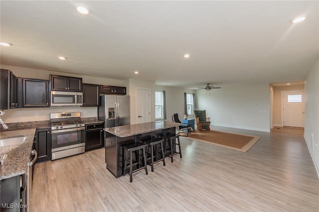 kitchen with light stone countertops, a kitchen island, stainless steel appliances, a breakfast bar, and light wood-type flooring