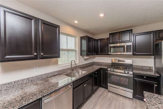 kitchen with dark stone countertops, appliances with stainless steel finishes, light wood-type flooring, and sink